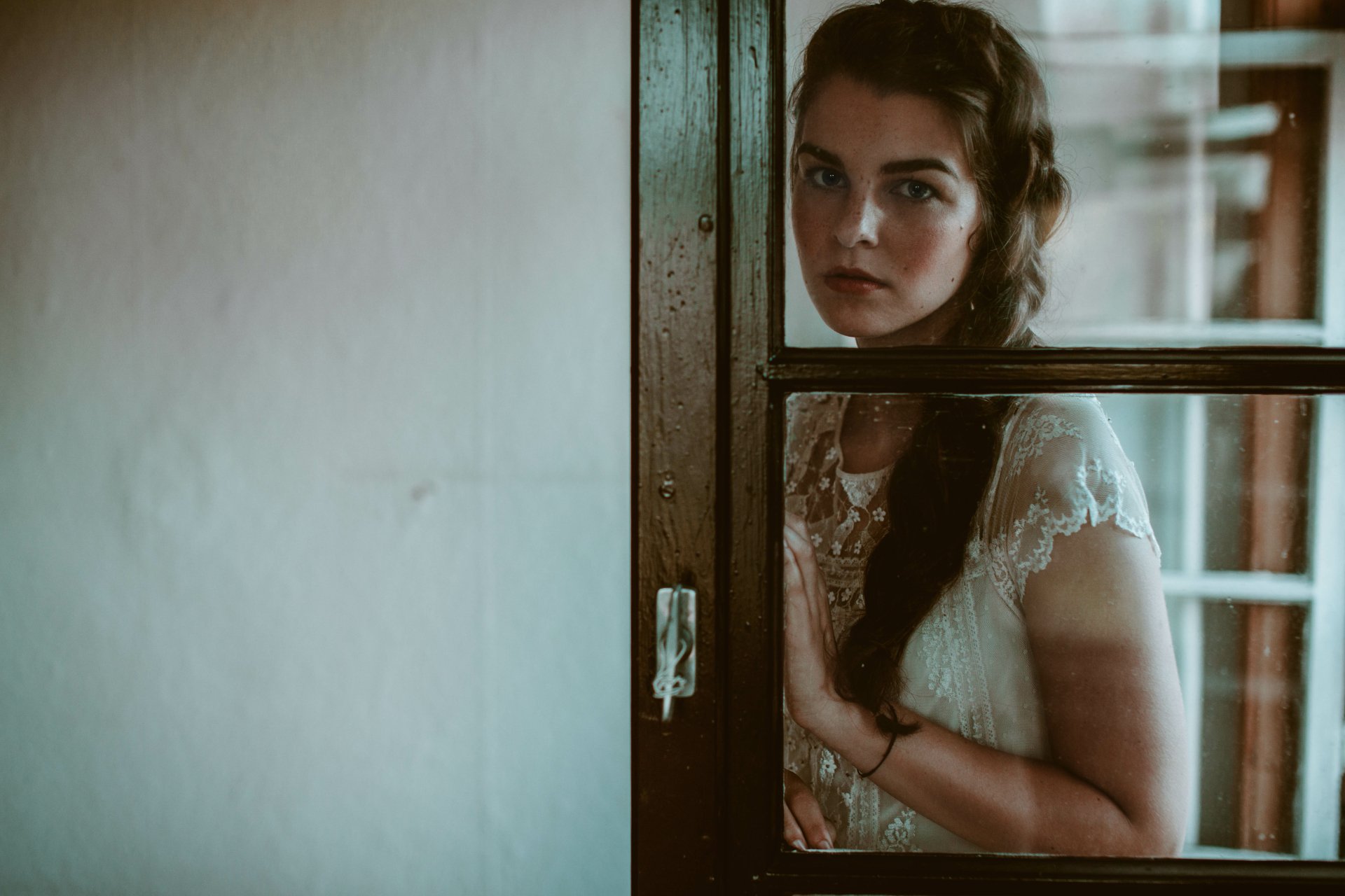 Brunette woman with a braid stands behind a glass window, captured in a soft, moody 4K Ultra HD desktop wallpaper and background.