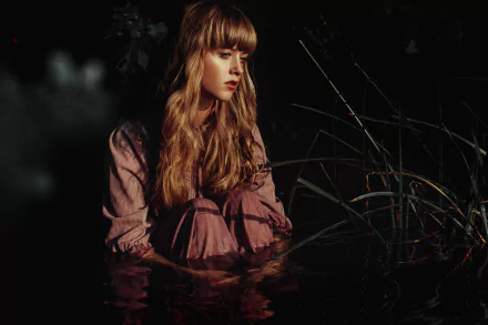 Blonde woman seated in dark water among reeds, moody lighting and reflective surface — 5K Ultra HD PC desktop wallpaper and background.