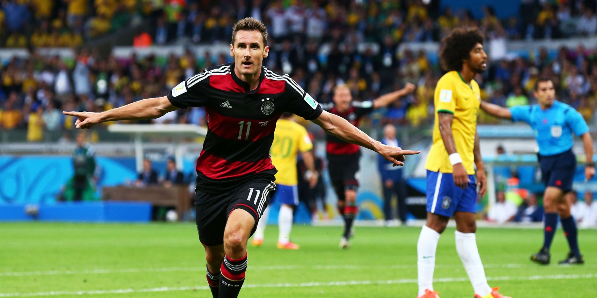 HD PC desktop wallpaper featuring an intense soccer match moment with a German player celebrating a goal, surrounded by Brazilian opponents in a vibrant stadium.