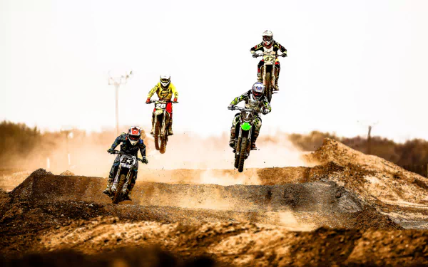 A dynamic motocross scene featuring four riders soaring through the air against a dusty background, showcasing the excitement and energy of the sport. HD desktop wallpaper.