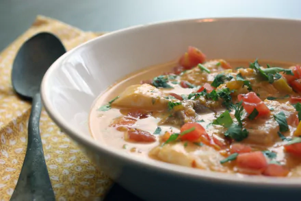 Close-up 4K Ultra HD PC desktop wallpaper of a creamy tomato and herb stew in a white bowl, garnished with chopped tomatoes and parsley beside a spoon on a yellow cloth.