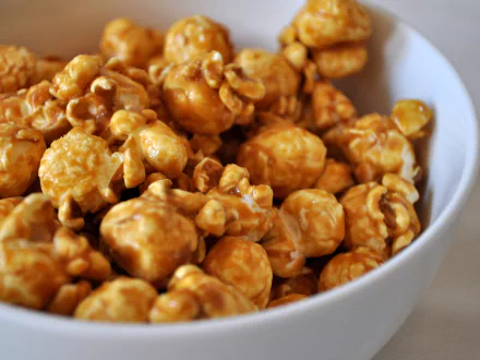 Close-up HD PC desktop wallpaper of caramel popcorn filling a white bowl, highlighting the glossy texture and rich golden color of the snack.