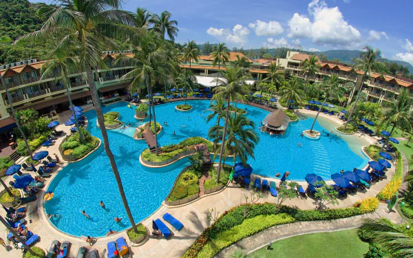 A vibrant resort in Phuket, Thailand features a large man-made pool surrounded by palm trees and lounge chairs, perfect for a holiday getaway. The scene captures a serene tropical paradise.