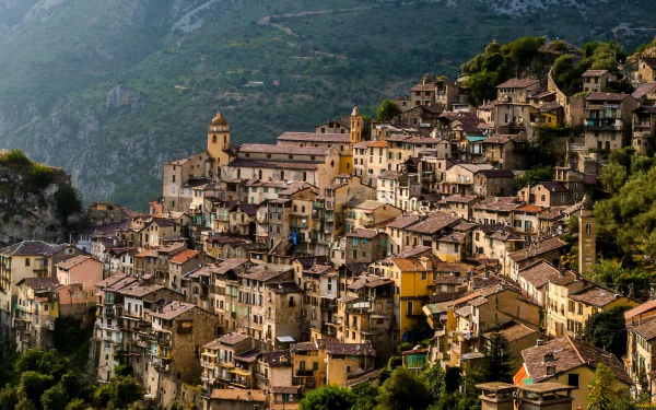 HD PC desktop wallpaper: Saorge, France — man-made hillside village of clustered stone houses and a church against green mountain slopes