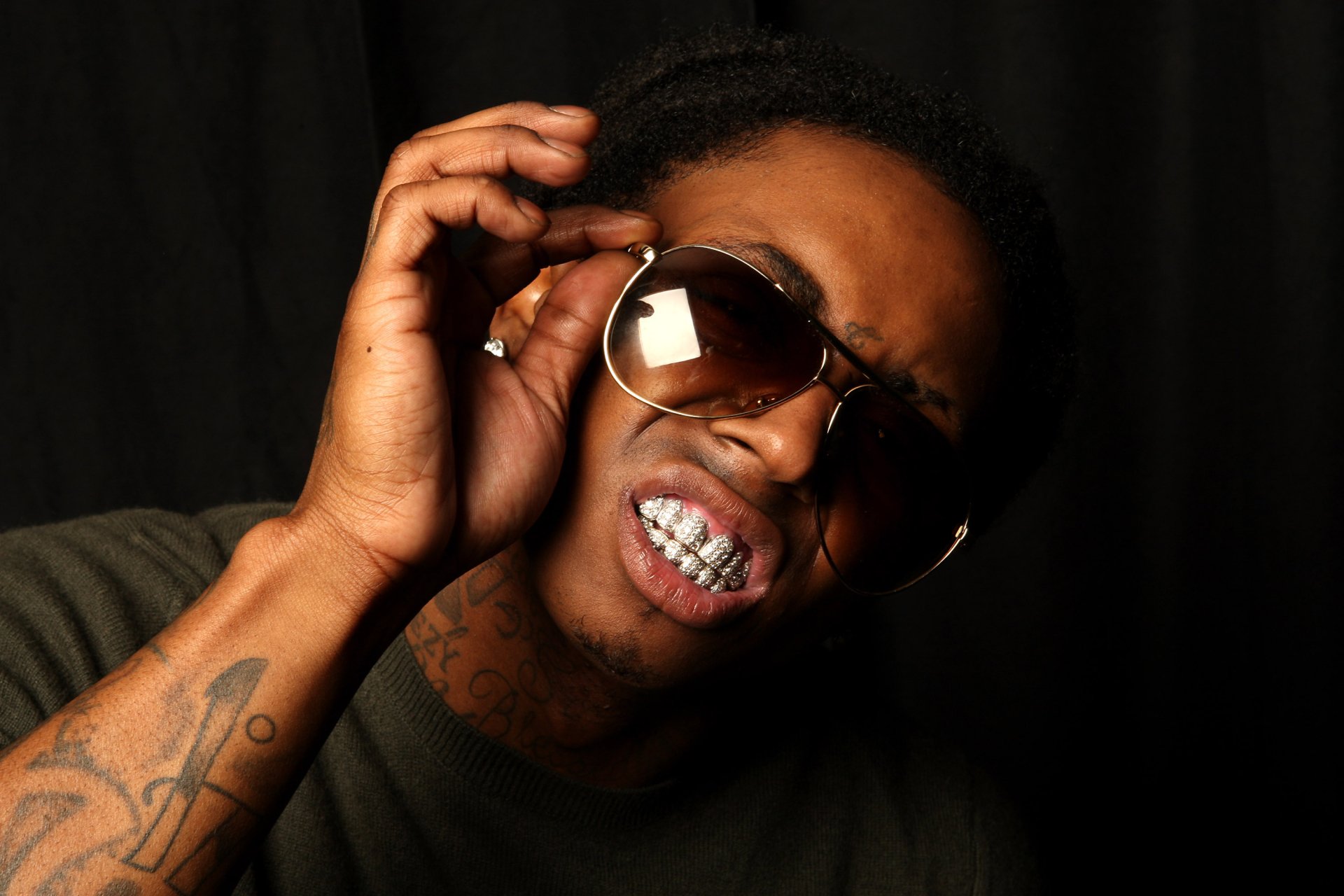 2K Quad HD PC desktop wallpaper: close-up portrait of a music artist/rapper with sunglasses, diamond grill and tattooed arm against a dark backdrop.