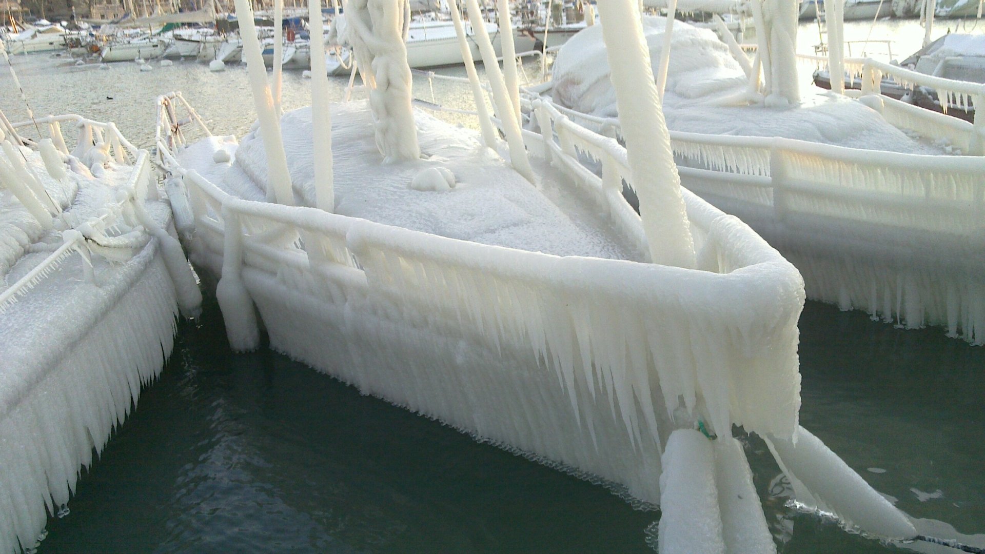 HD desktop wallpaper: winter photography of moored boats and dock coated in thick ice with long icicles hanging over dark harbor water.