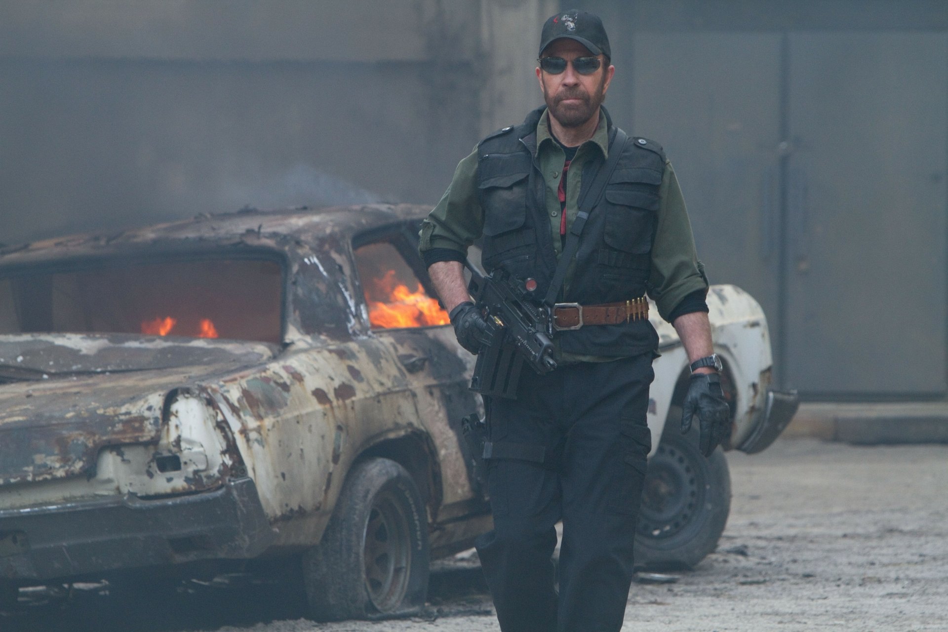 Chuck Norris as Booker from The Expendables 2 walks confidently in a fiery, war-torn urban setting. 4K Ultra HD PC desktop wallpaper and background.