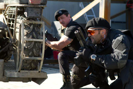 5K Ultra HD PC wallpaper from The Expendables 2: two armed mercenaries crouch behind wreckage, one aiming a pistol while the other scans the area in sunglasses and tactical gear.