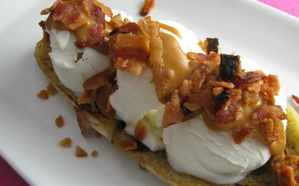 HD desktop wallpaper featuring a close-up of a banana split topped with whipped cream, caramel sauce, and crispy bacon bits.