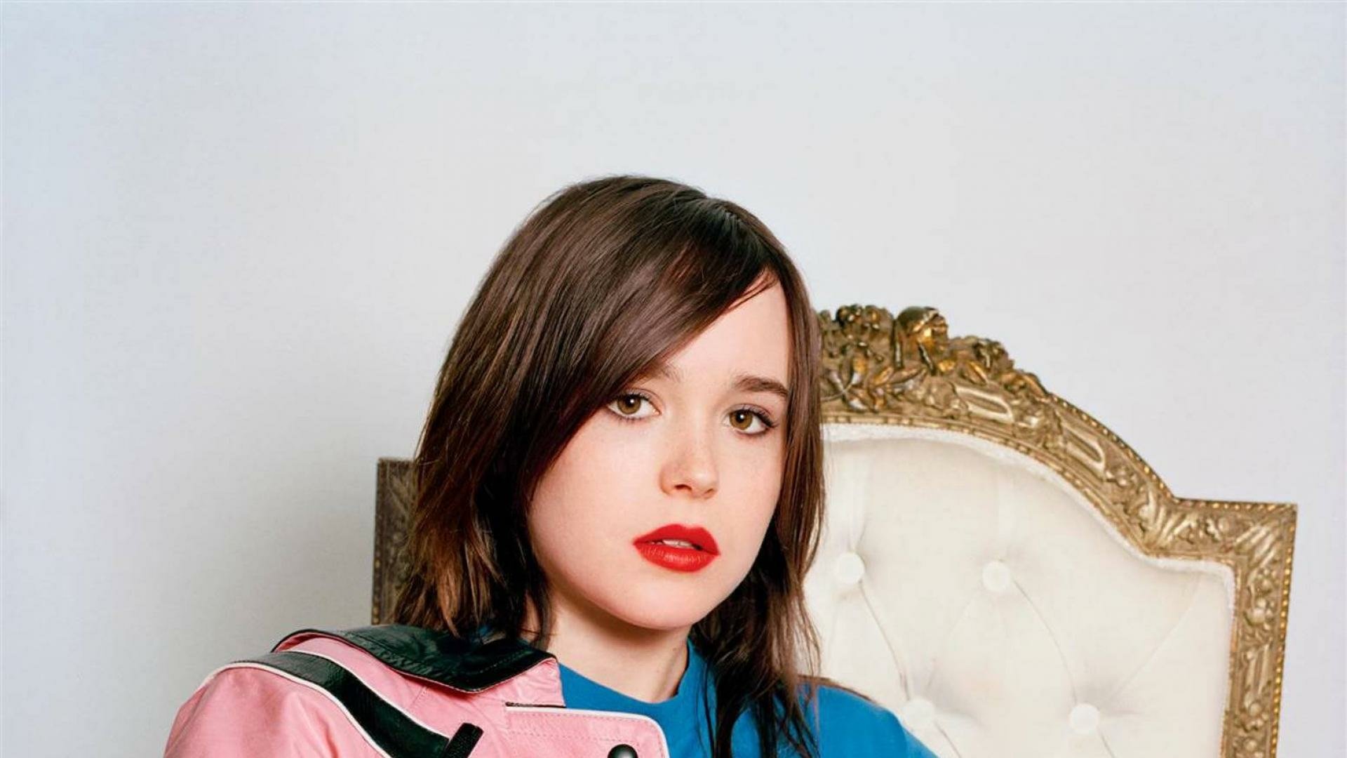 HD PC desktop wallpaper: celebrity portrait (identity unspecified) of a young woman with short dark hair and red lipstick, wearing a pink-and-blue jacket, seated on an ornate white chair.