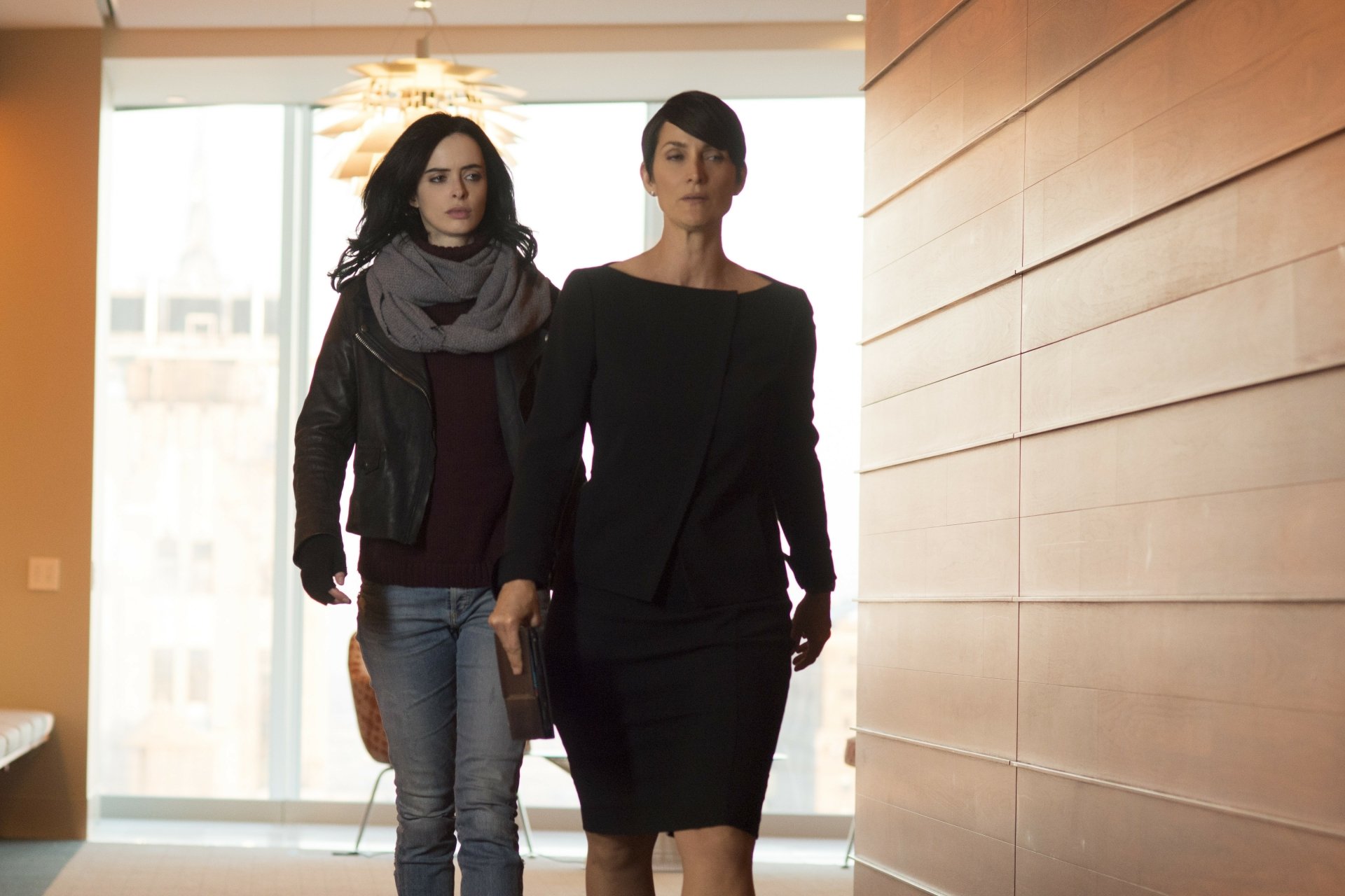 Jeryn Hogarth and Jessica Jones from the TV show Jessica Jones stride confidently down a modern hallway — moody 4K Ultra HD desktop wallpaper.