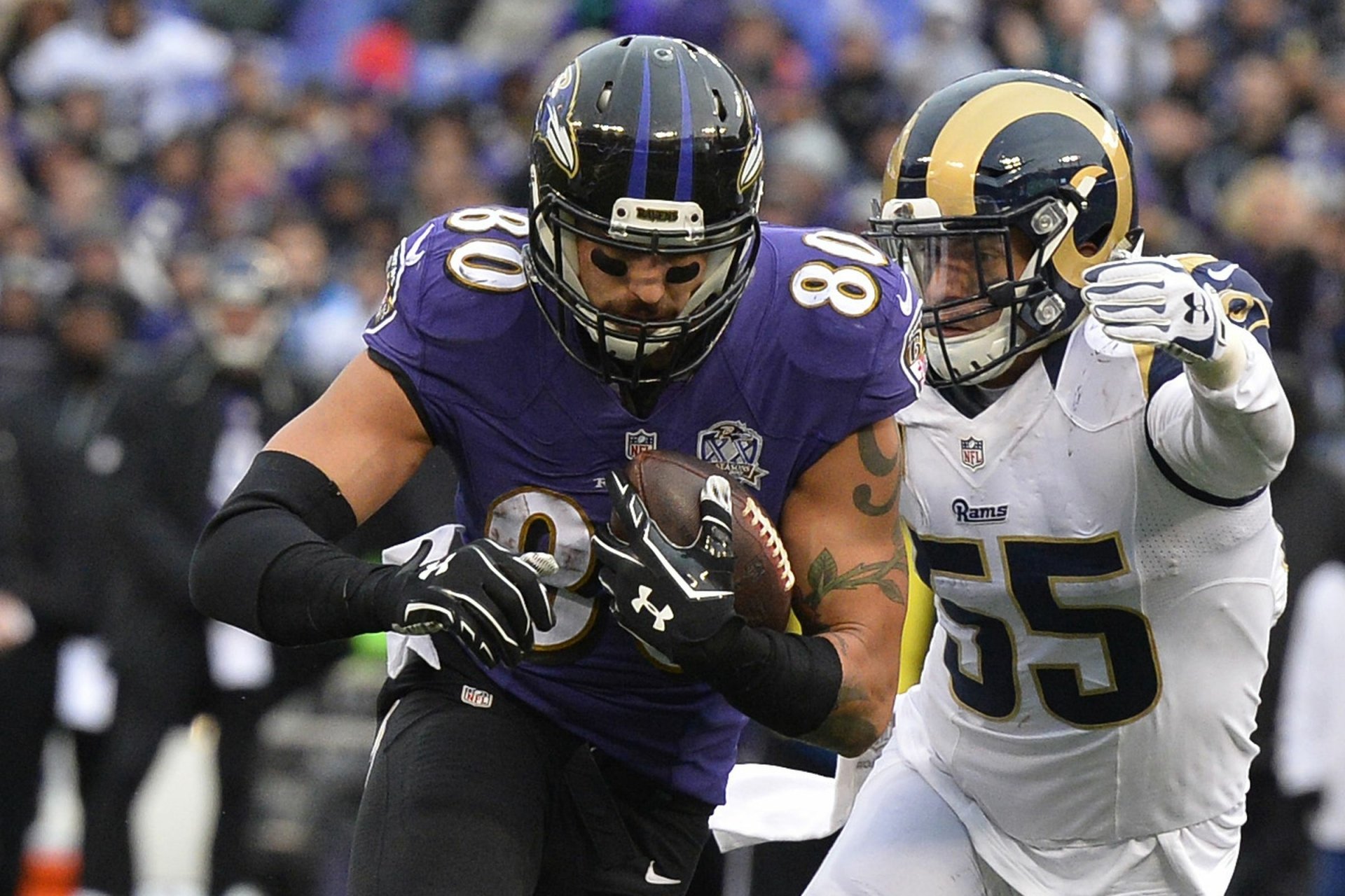 HD PC desktop wallpaper: Baltimore Ravens player carrying the ball as an opposing defender attempts a tackle in a high-energy NFL sports action shot.