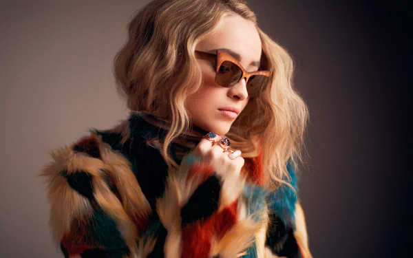 Blonde singer Sabrina Carpenter poses in stylish sunglasses and a colorful fur coat, captured in a vibrant HD desktop wallpaper.