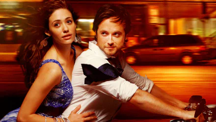 Fiona Gallagher and Jimmy Lishman from the TV show Shameless embrace in a vibrant, dynamic scene, set against a backdrop of city lights, creating a striking HD desktop wallpaper.