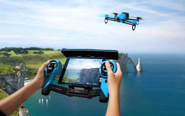 A person controls a drone with a blue remote display overlooking a stunning coastline, featuring cliffs and vibrant greenery. This 4K Ultra HD image captures an exhilarating outdoor moment.