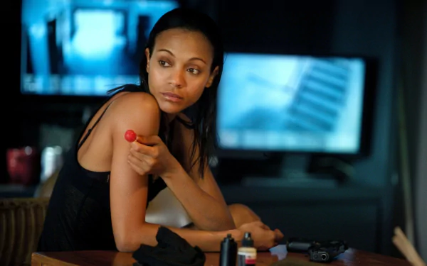 Zoe Saldana in a scene from the movie *Colombiana*, featuring her poised with a red lollipop, set against a backdrop of screens offering a cinematic atmosphere.