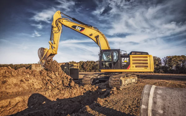 4K Ultra HD desktop wallpaper featuring a yellow Caterpillar Inc. excavator digging earth under a dramatic cloudy sky at a construction site.