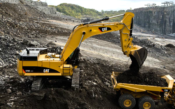 A Caterpillar Inc. excavator loads dirt into a dump truck at a rocky mining site, captured in high detail for 4K Ultra HD PC desktop wallpaper and background.