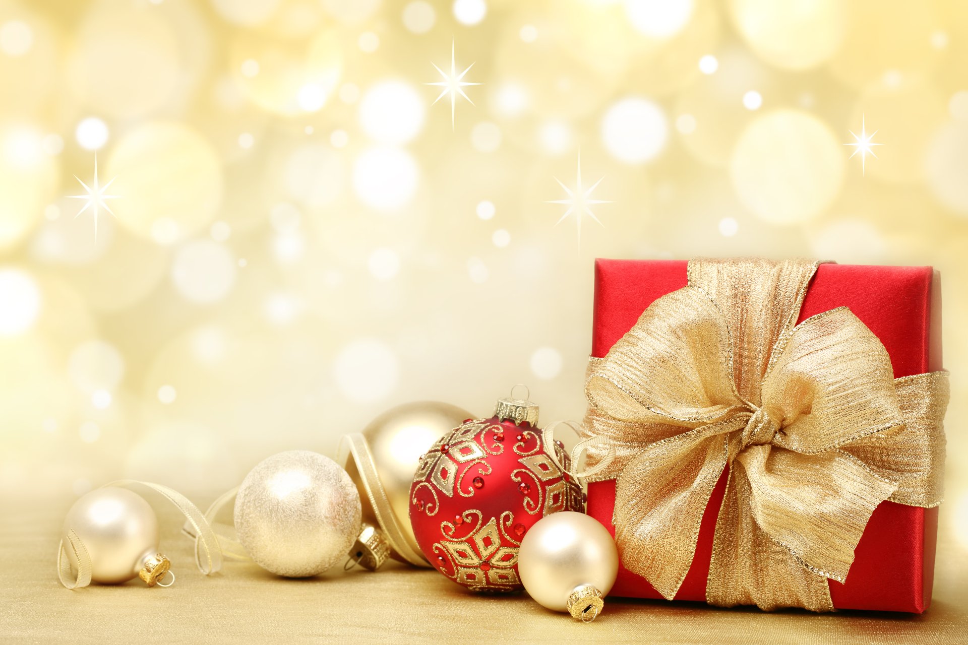 A 4K Ultra HD desktop wallpaper featuring a red gift box with a large gold ribbon, surrounded by gold and red Christmas ornaments against a glowing holiday background.