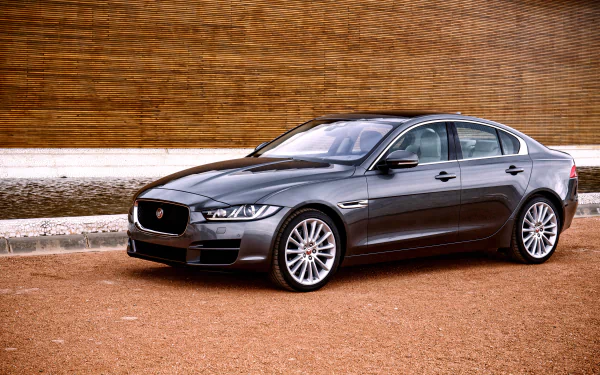 Silver Jaguar XE sedan parked on a gravel surface with a wooden wall backdrop, captured in 4K Ultra HD for a PC desktop wallpaper and background.
