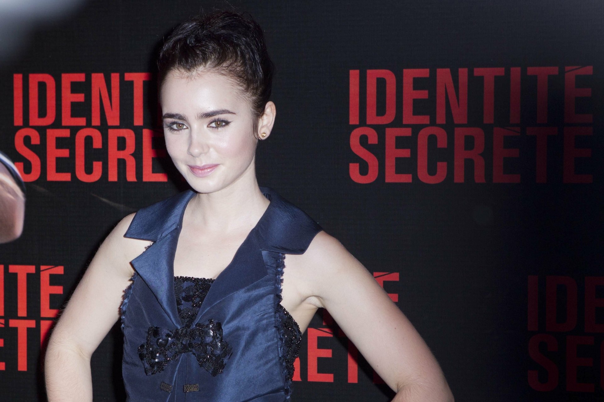 Portrait of an actress posing at a red-and-black Identité Secrète premiere backdrop; high-resolution 2K Quad HD PC desktop wallpaper/background.