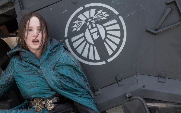 A dramatic scene featuring Jennifer Lawrence in a vibrant teal outfit, from The Hunger Games: Mockingjay - Part 2, set against a striking background with a symbol of rebellion.