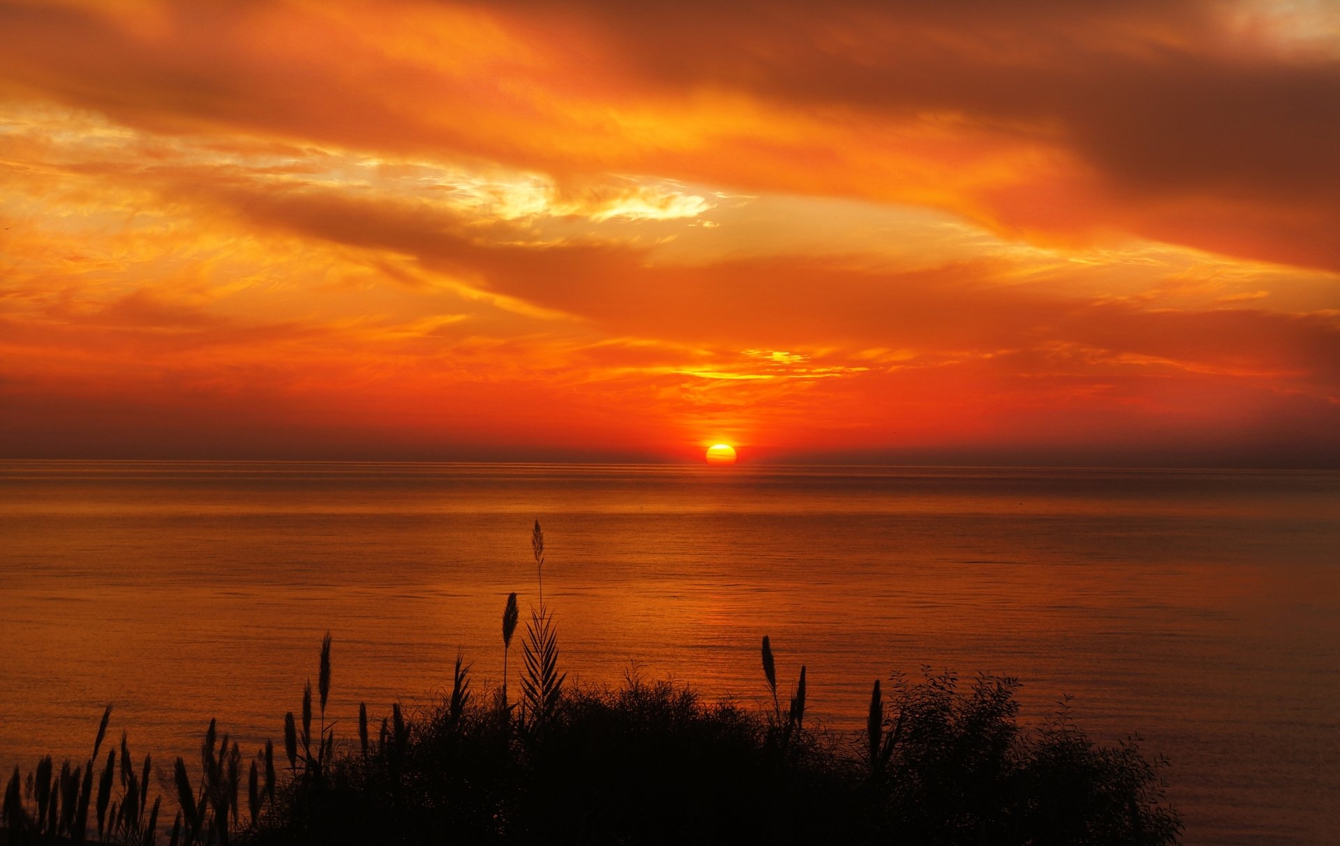 A breathtaking sunset over the ocean, featuring vibrant orange and yellow hues blending into the sky, with clouds reflecting the colors at the horizon, showcasing serene nature.