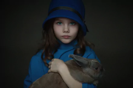 A portrait of a child with blue eyes and brunette hair, wearing a blue hat and coat, holding a rabbit. The dark background enhances the focus on the child and rabbit. HD desktop wallpaper and background.