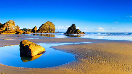 HD PC desktop wallpaper: blue coastal nature scene with sunlit sea stacks, reflective tidal pools and a sandy beach under a clear sky.