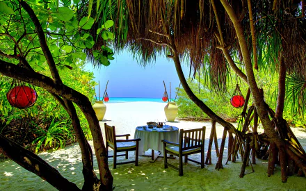 A serene tropical setting in the Maldives features a beautifully arranged table under lush greenery, with a stunning beach view in the background, capturing the essence of a relaxing holiday.