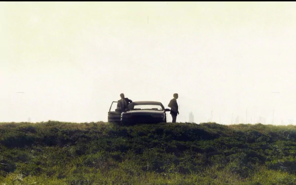 HD PC desktop wallpaper featuring a scene from the TV show True Detective, with two figures standing near a car on a grassy hill under a pale sky.
