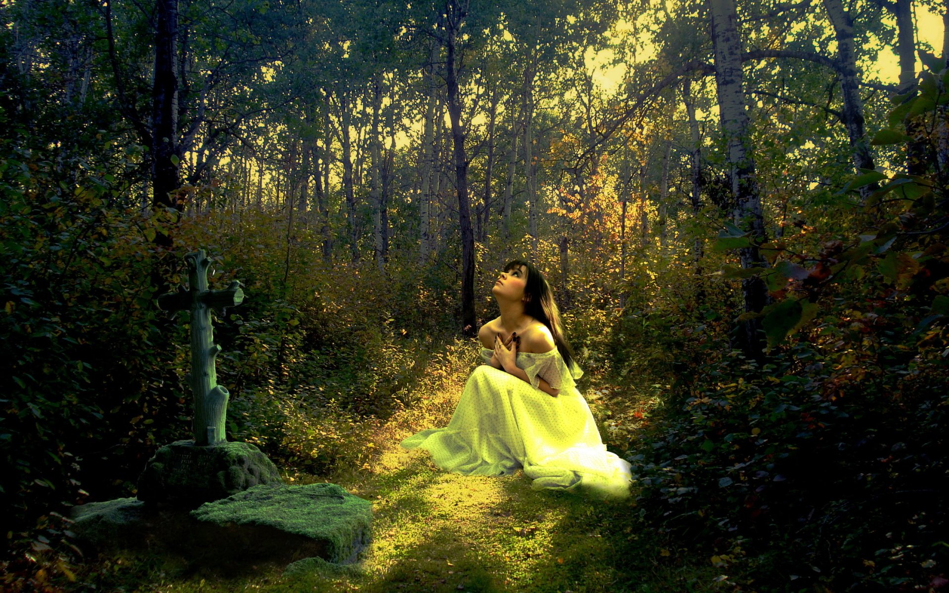 A woman in a white dress kneels in a forest beside a grave with a cross, bathed in dappled sunlight. The image conveys a serene and contemplative mood, captured in high definition as a desktop wallpaper.