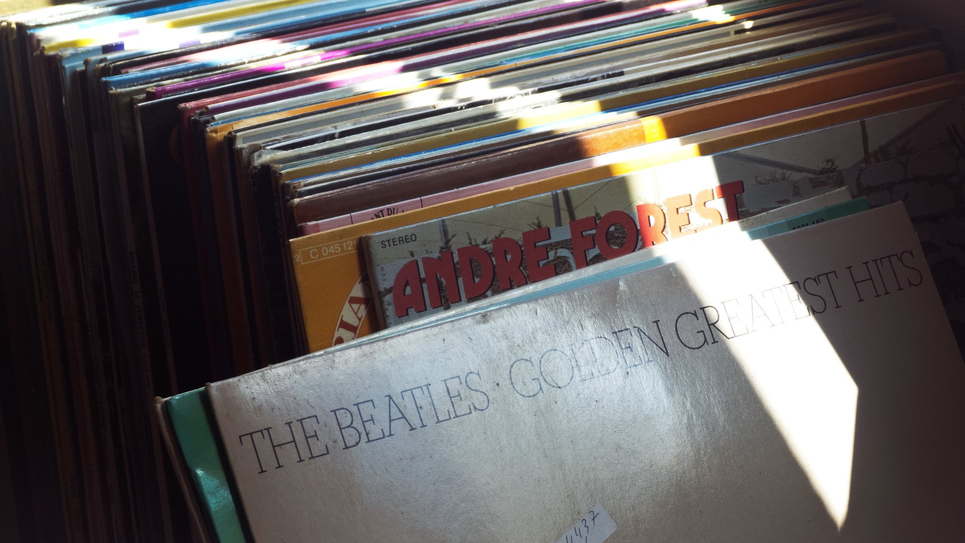 Sunlit close-up of stacked vinyl records with a worn 'The Beatles' album in front; music record collection, 4K Ultra HD PC desktop wallpaper.