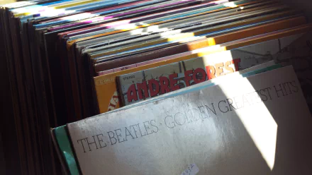 Sunlit close-up of stacked vinyl records with a worn 'The Beatles' album in front; music record collection, 4K Ultra HD PC desktop wallpaper.