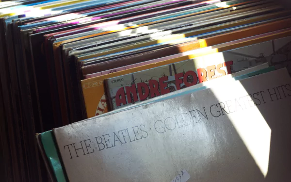 Sunlit close-up of stacked vinyl records with a worn 'The Beatles' album in front; music record collection, 4K Ultra HD PC desktop wallpaper.