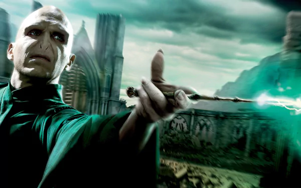 HD PC desktop wallpaper of Lord Voldemort from Harry Potter and the Deathly Hallows: Part 2, casting green magic with a ruined Hogwarts battlefield looming behind him.