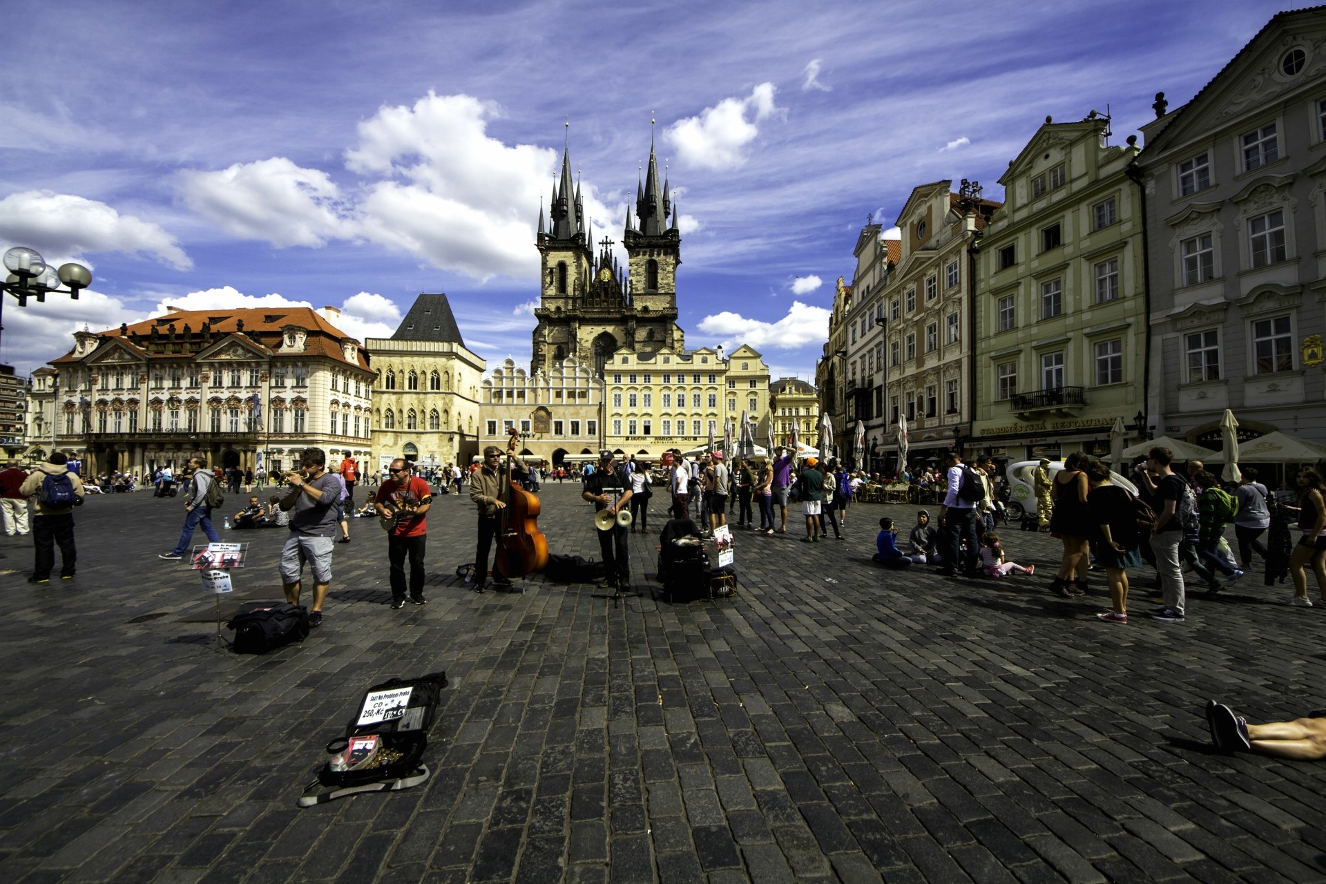 5K Ultra HD PC wallpaper: Prague Old Town Square, man-made Gothic towers and pastel buildings, cobblestone plaza with street performers and crowds under a vivid blue sky.