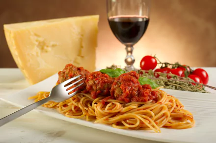 A delicious plate of spaghetti topped with meatballs and tomato sauce, accompanied by cheese, fresh tomatoes, and a glass of red wine, all set against a warm background.