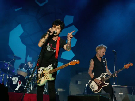 HD desktop wallpaper featuring Billie Joe Armstrong and Green Day performing live on stage with guitars under blue lighting.