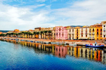 Vibrant colorful houses line a canal in a Sardinian town, Italy, with boats moored along the waterfront under a bright sky, captured in an HD desktop wallpaper.