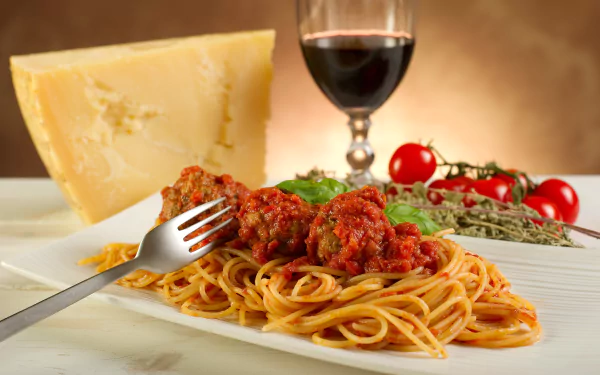 A delicious plate of spaghetti topped with meatballs and tomato sauce, accompanied by cheese, fresh tomatoes, and a glass of red wine, all set against a warm background.