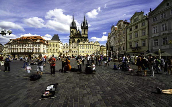5K Ultra HD PC wallpaper: Prague Old Town Square, man-made Gothic towers and pastel buildings, cobblestone plaza with street performers and crowds under a vivid blue sky.