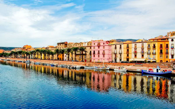 Vibrant colorful houses line a canal in a Sardinian town, Italy, with boats moored along the waterfront under a bright sky, captured in an HD desktop wallpaper.