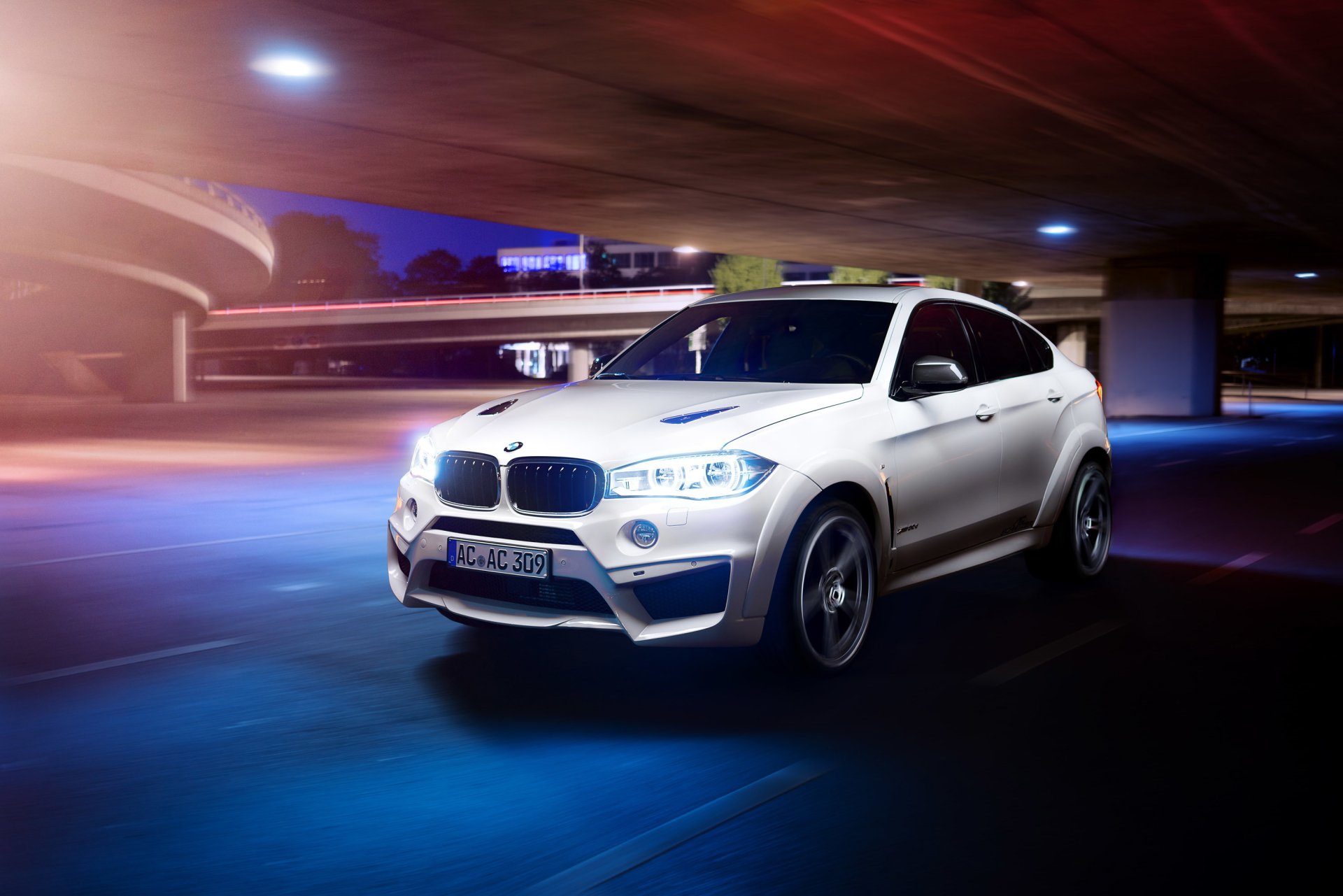 A white BMW X6 SUV driving at night under a curved overpass, captured in a dynamic HD desktop wallpaper showcasing the vehicle's sleek design.