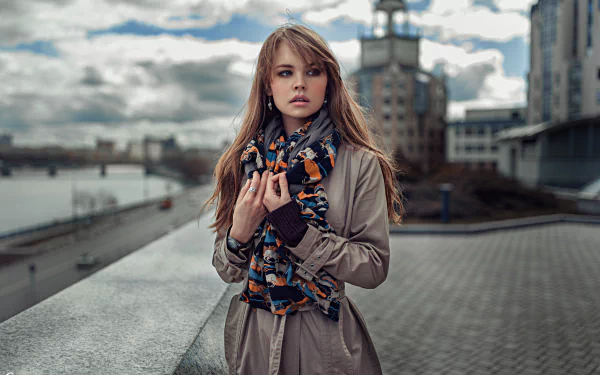 Brunette woman wearing a scarf, standing outdoors against a cityscape bokeh background. The image is a HD desktop wallpaper featuring model Anastasiya Scheglova.