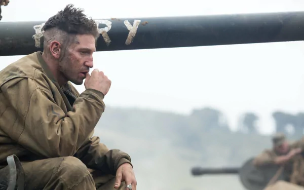 A contemplative Jon Bernthal sits beside a tank in a scene from the movie Fury, set against a dramatic battlefield backdrop, creating an intense HD desktop wallpaper.