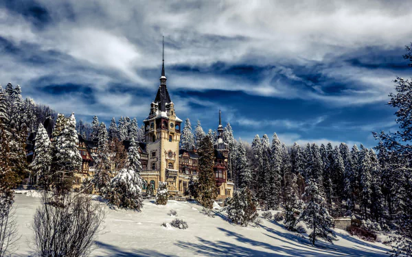 Peles Castle in winter, surrounded by snow-covered forest under a dramatic sky in Romania.