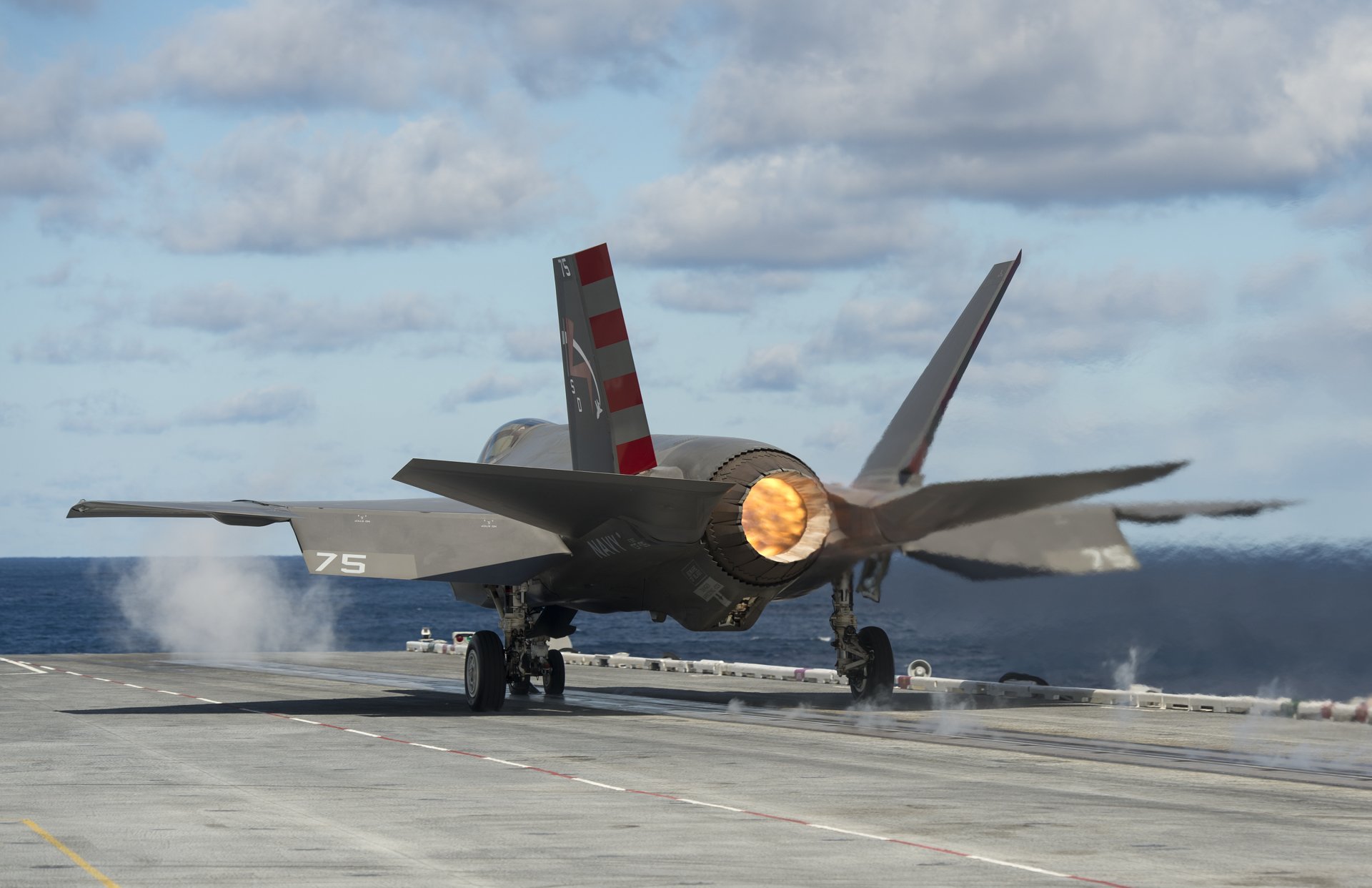 Lockheed Martin F-35 Lightning II jet fighter, a military warplane, captured from behind during takeoff on a runway under a partly cloudy sky.