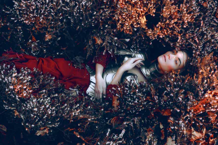 A woman model lies amidst dense, dark plants wearing armor, creating a moody atmosphere in this HD PC desktop wallpaper.