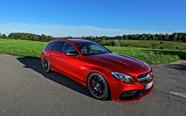 HD desktop wallpaper featuring a red Mercedes-Benz C-Class car parked on a paved road with green fields and a clear blue sky in the background.